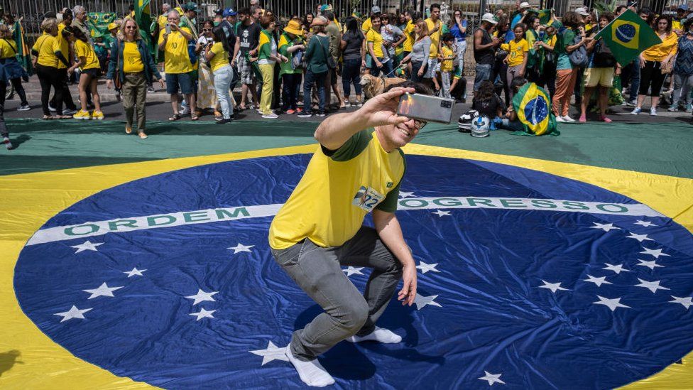 A supporter of the current president of Brazil and candidate for re-election, Jair Bolsonaro standing on a Brazilian flag, takes a selfie during a campaign rally on Brazil's 200th Independence day events