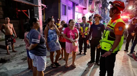 EPA A man wearing a high-viz vest and helmet speaks to a group of people