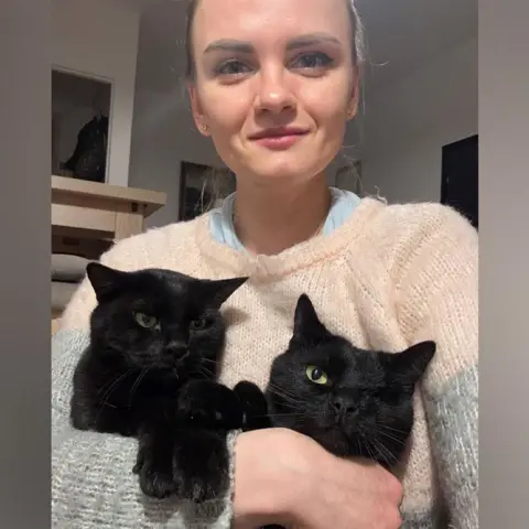 Handout A woman with blonde hair holds two black cats